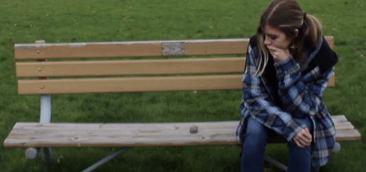 woman contemplating a rock that is "sitting" on a park bench beside her