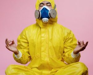person in yellow bio suit with double-filter mask, in meditation position