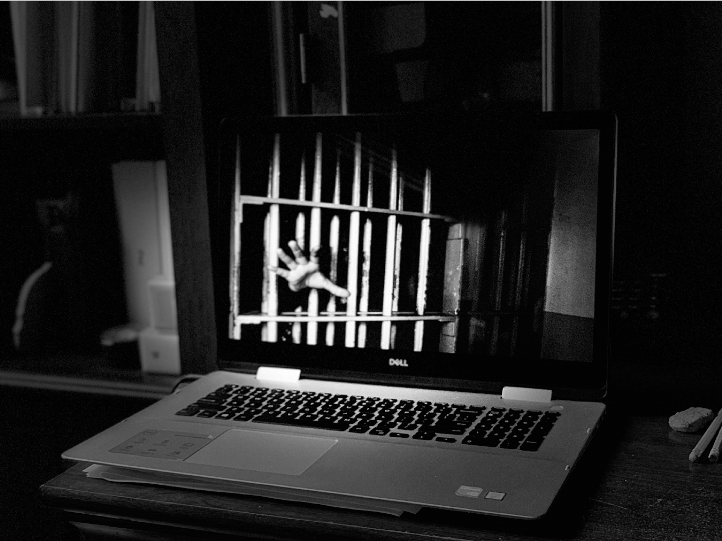 black and white image on computer laptop: hand reaching through bars