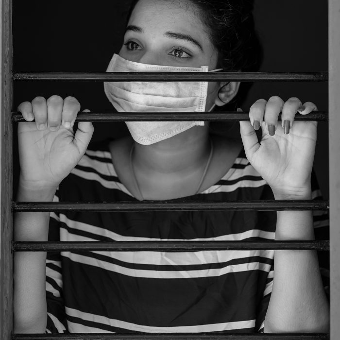 young woman in medical mask behind horizontal bars