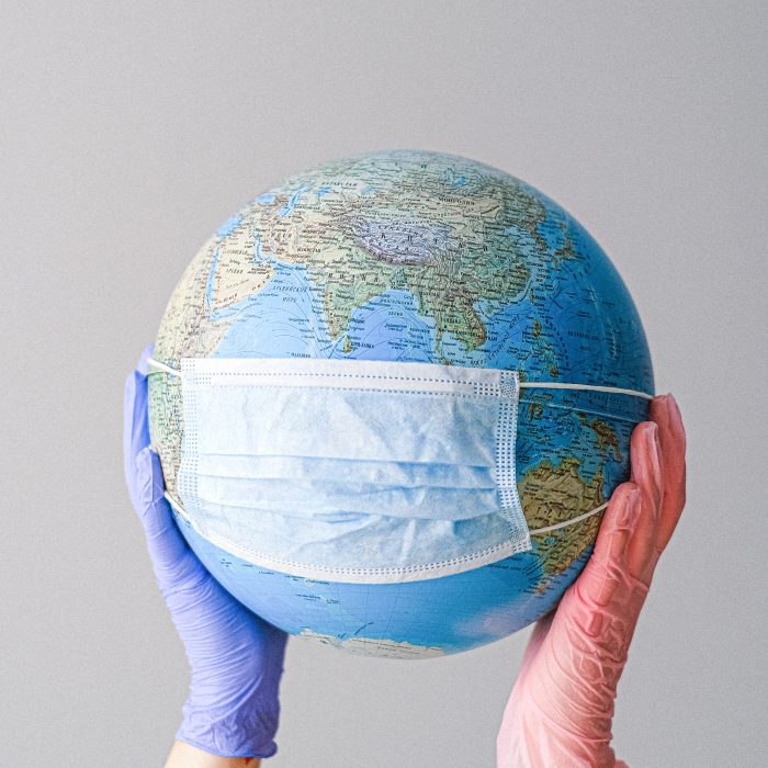 hands in medical gloves holding globe that is wearing medical mask